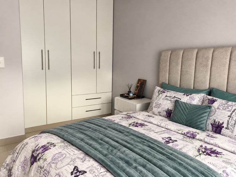 A well-maintained bedroom featuring a large white built-in wardrobe with integrated drawers and neutral tiled flooring.