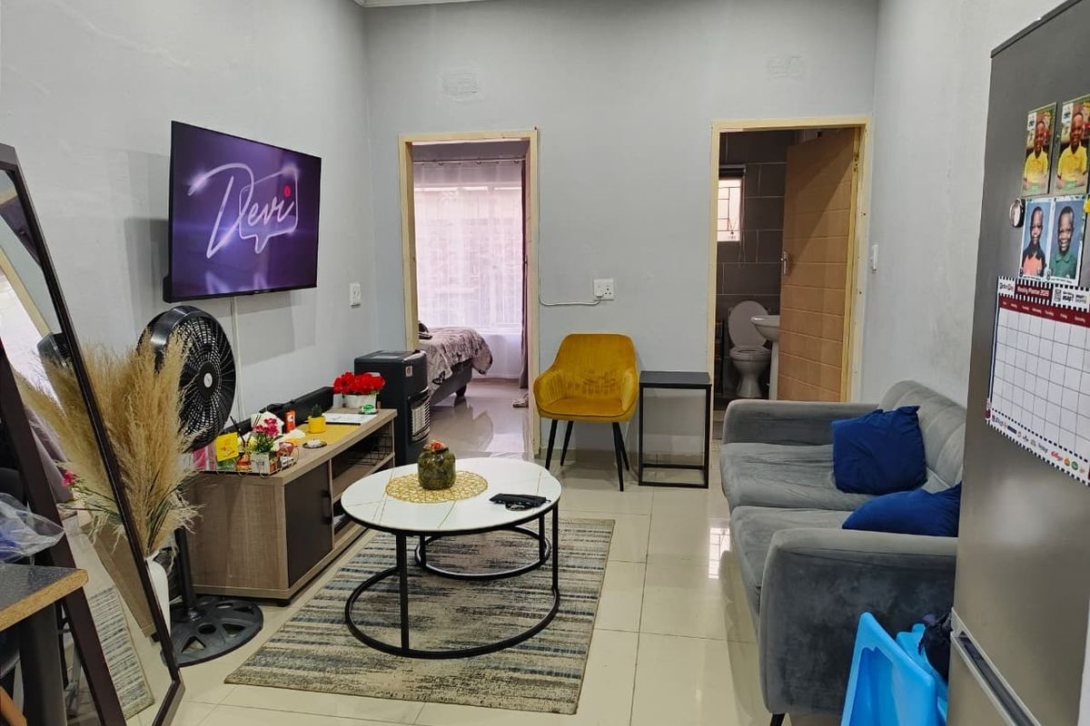 A compact living room featuring tiled flooring and neutral wall finishes, providing access to adjacent bedroom and bathroom areas.
