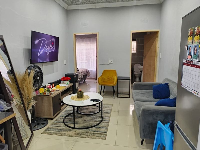 A compact living room featuring tiled flooring and neutral wall finishes, providing access to adjacent bedroom and bathroom areas.