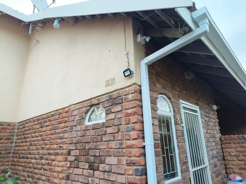Exterior view of the apartment entrance featuring a brick and plaster facade, security gate, and exposed roof rafters.