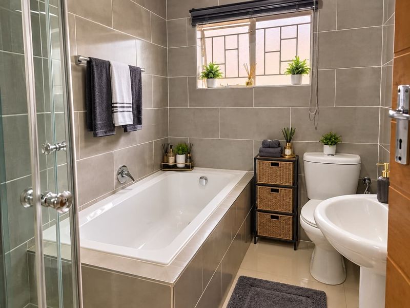 Modern bathroom featuring a built-in bathtub, pedestal sink, toilet, and a glass-enclosed shower, finished with neutral ceramic wall tiles.