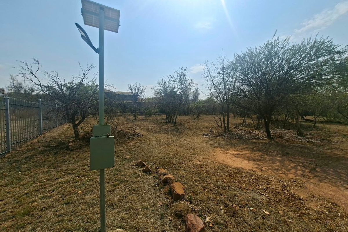 A vacant residential plot featuring mature trees, perimeter fencing, and a solar-powered light fixture.