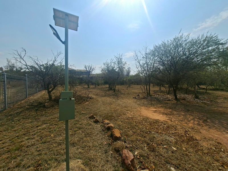 A vacant residential plot featuring mature trees, perimeter fencing, and a solar-powered light fixture.