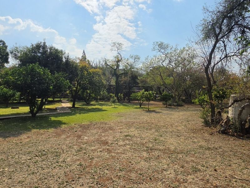 A spacious, established farm garden featuring mature trees, a well-maintained lawn, and a paved pathway leading through the grounds.