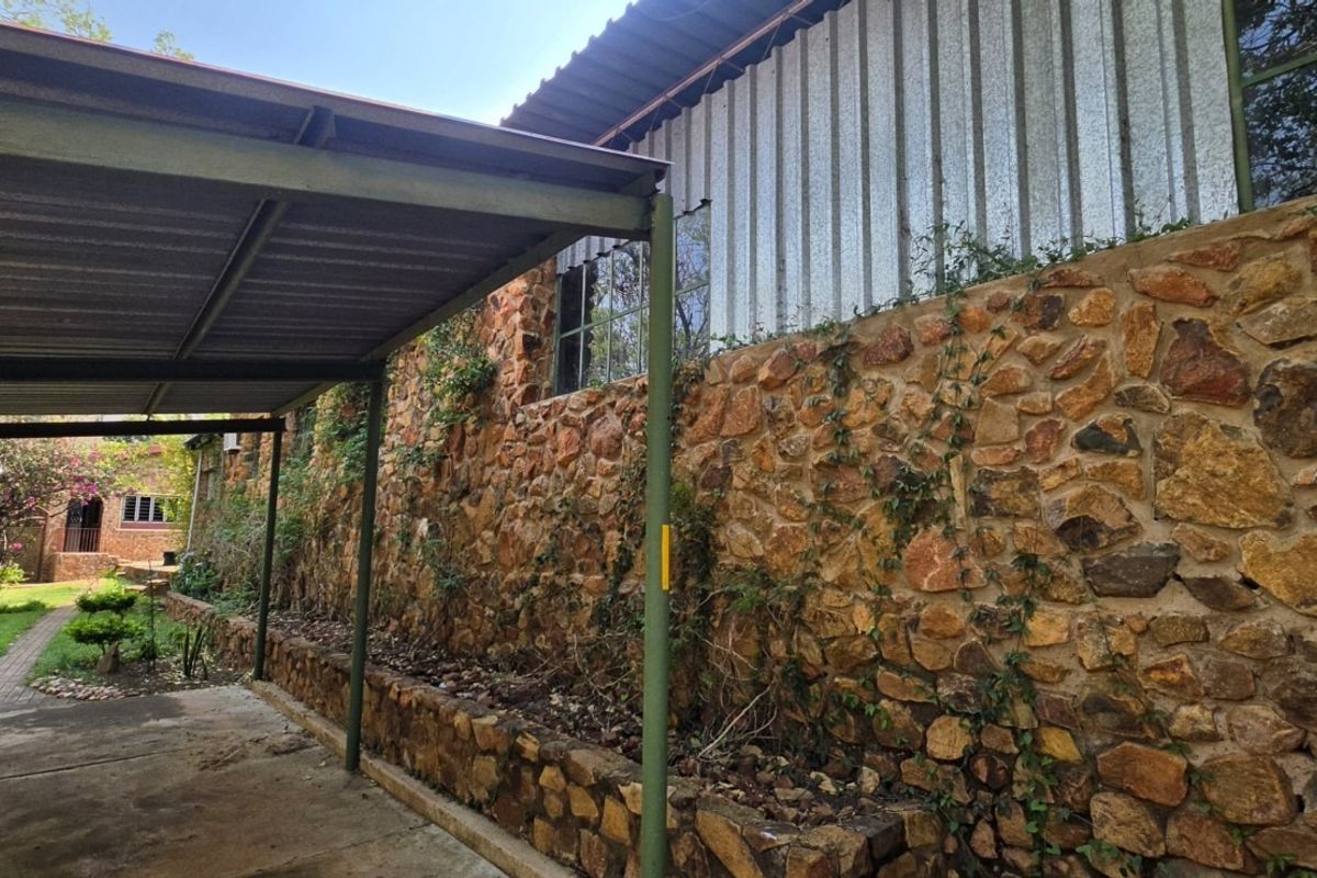 Rear exterior view of the farm property featuring a stone-clad wall, corrugated metal roofing, and a covered carport area adjacent to a garden path.
