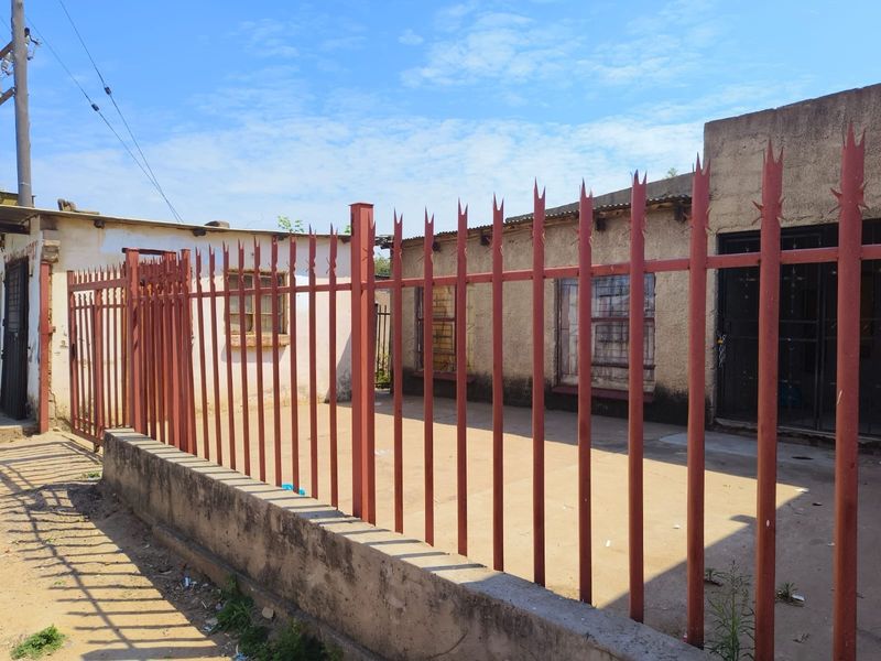 Front exterior view of the property featuring a concrete driveway, secured by a metal spike fence and a gated entrance.