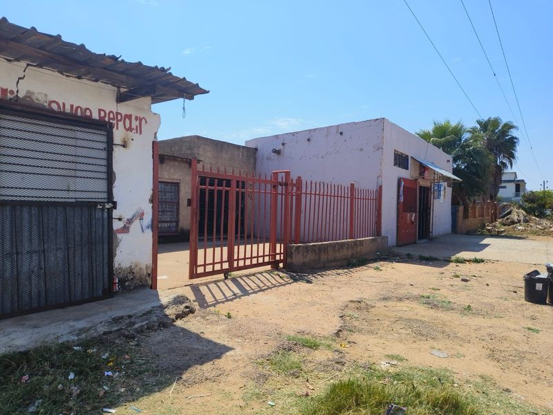 Front exterior view of a property featuring a metal security gate, fencing, and masonry structures requiring significant maintenance and exterior repairs.