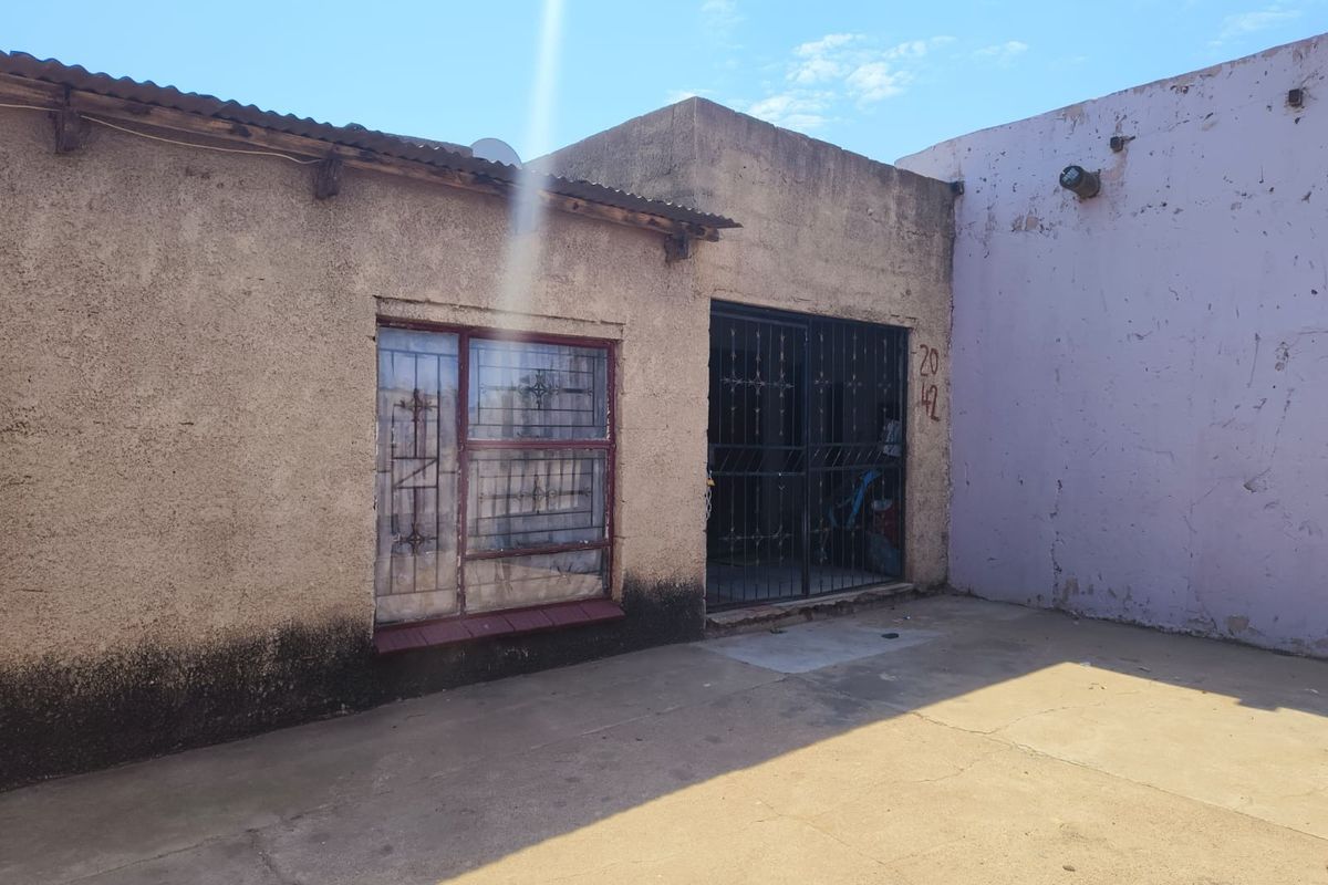 Front exterior view of the property featuring a concrete paved area, security gate, and security bars on the window.