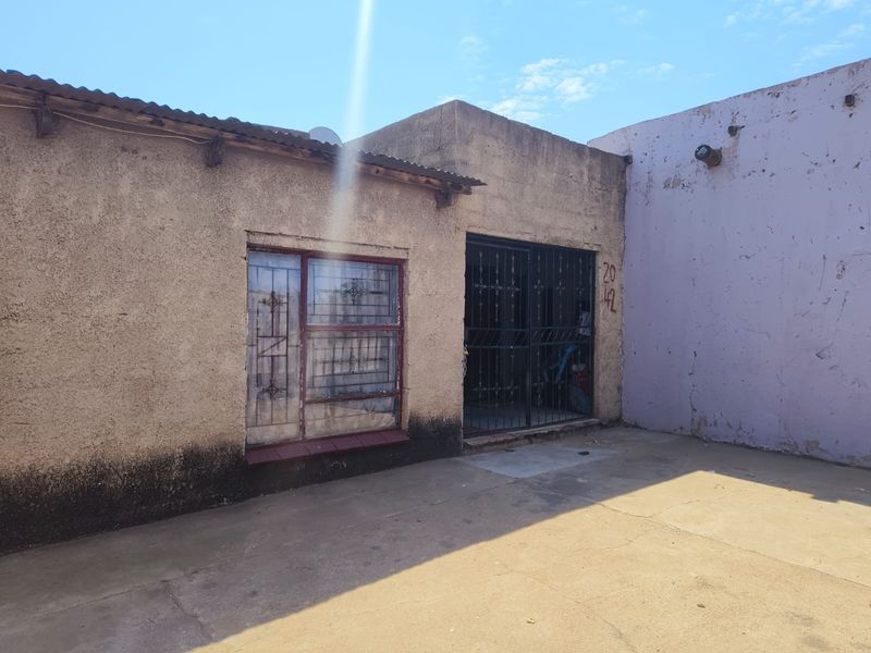 Front exterior view of the property featuring a concrete paved area, security gate, and security bars on the window.