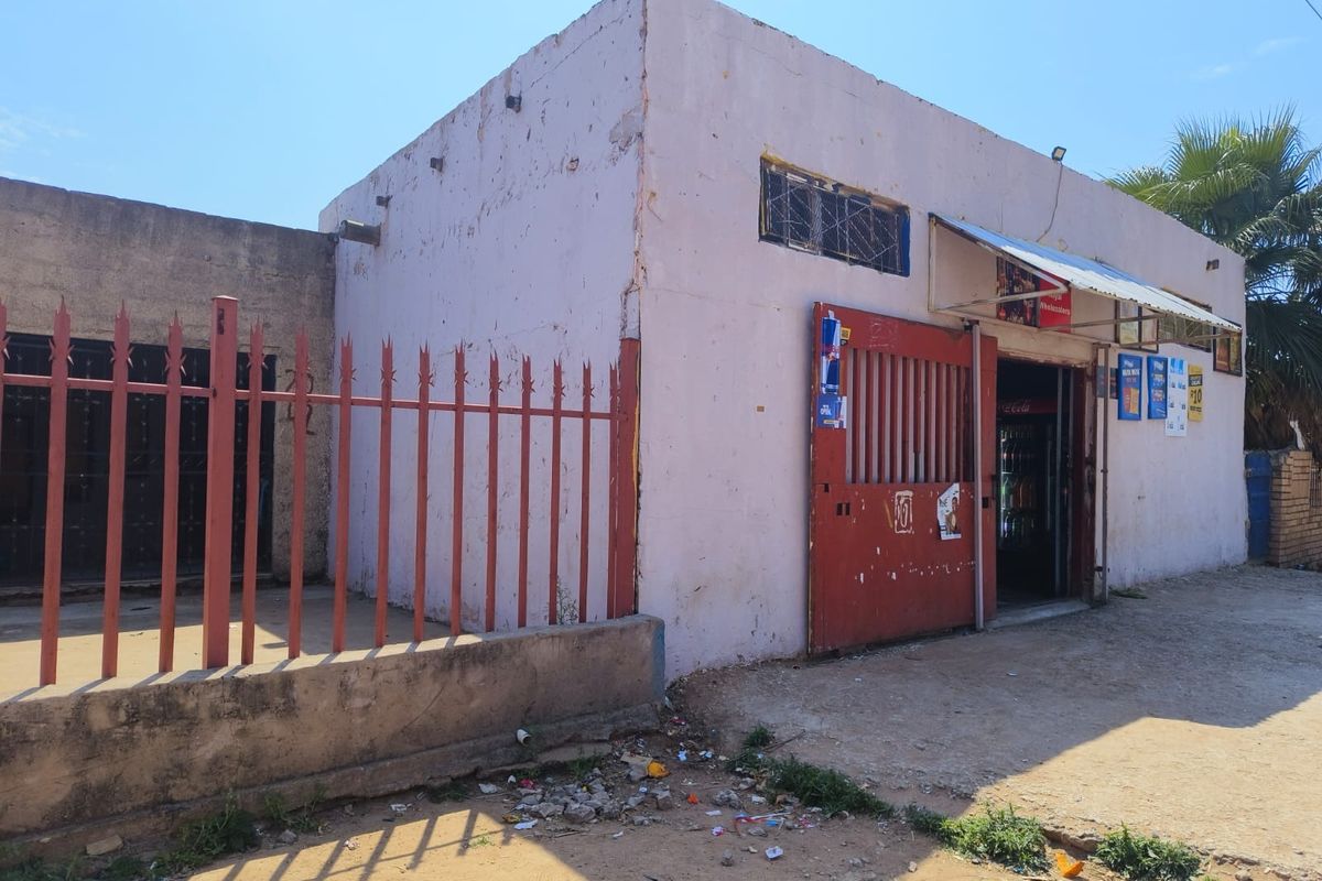 Front exterior view of a commercial-style building featuring a metal security gate, perimeter fencing, and a weathered concrete facade.
