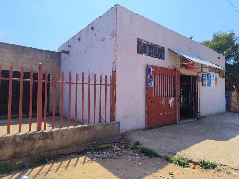Front exterior view of a commercial-style building featuring a metal security gate, perimeter fencing, and a weathered concrete facade.