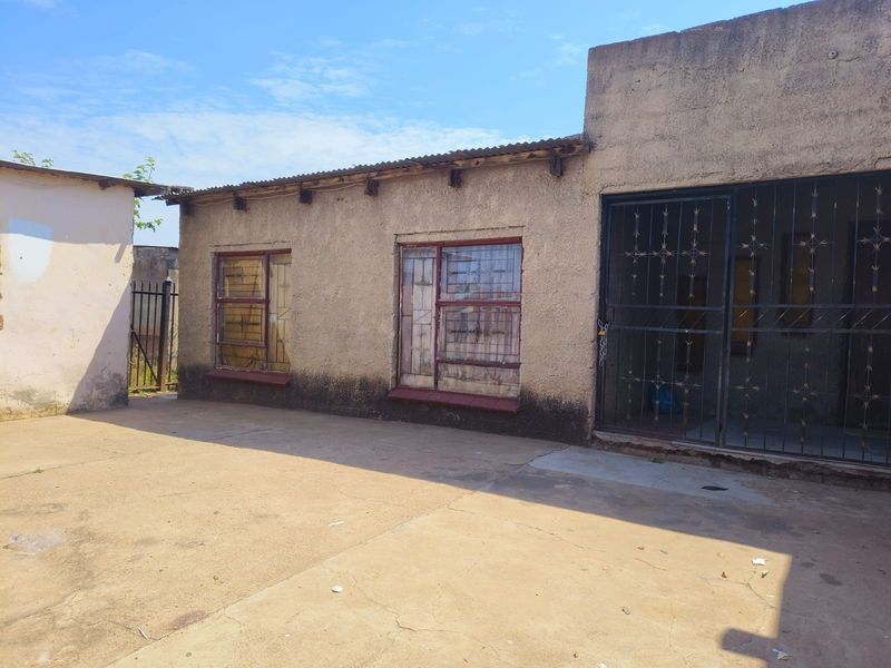 Rear exterior view of the property featuring a concrete paved yard, security gates, and weathered wall finishes.