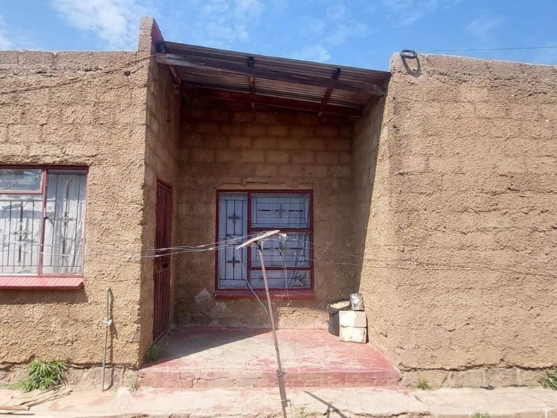 Front elevation of a single-story house featuring a textured render finish, metal window frames with security bars, and a covered entrance porch.