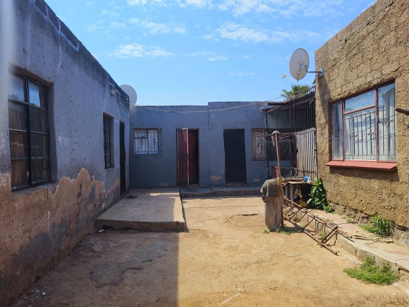 Rear courtyard area featuring concrete paving, security gates, and steel window frames, requiring maintenance to the exterior wall finishes.