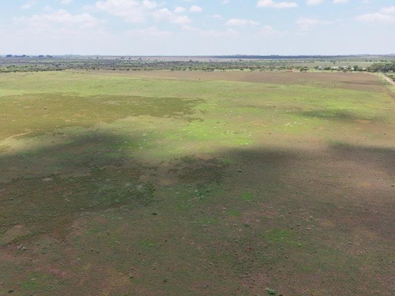 An expansive aerial view of open farm land featuring natural vegetation, perimeter fencing, and visible power lines stretching across the landscape.