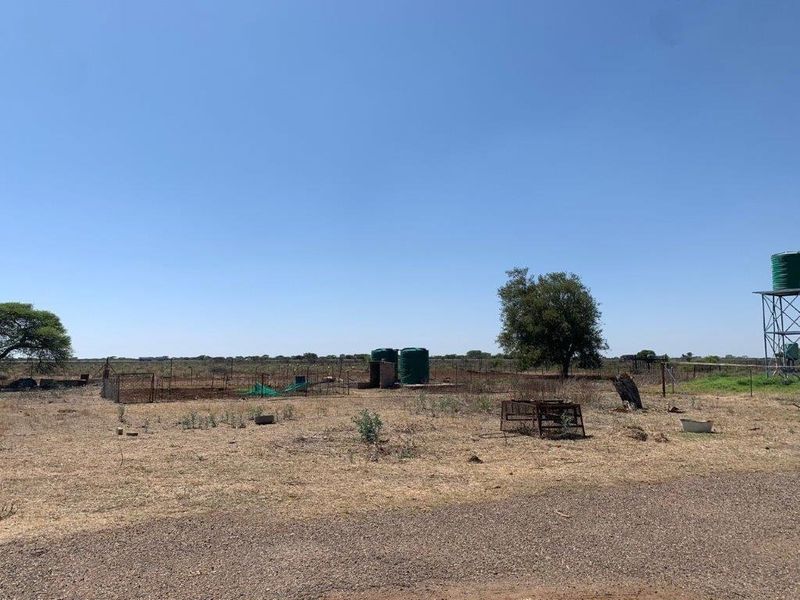 Expansive farm land featuring water storage tanks, an elevated tank stand, and perimeter wire fencing under a clear sky.