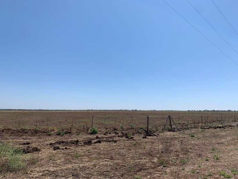A wide-angle view of open farmland featuring wire fencing and expansive, flat terrain under a clear blue sky.