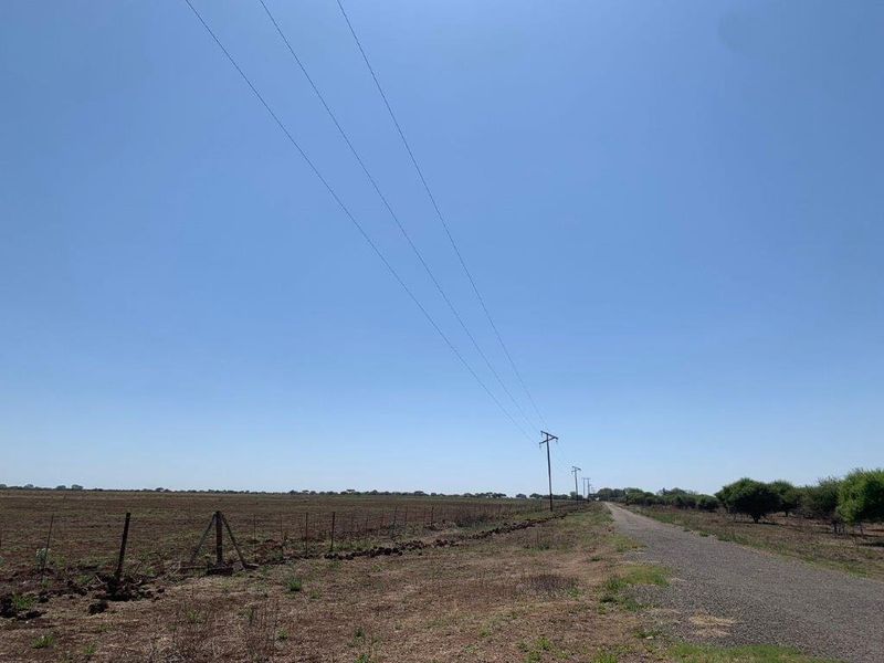 A view of the farm property showing a gravel access road, wire fencing, and overhead power lines stretching across the open landscape.