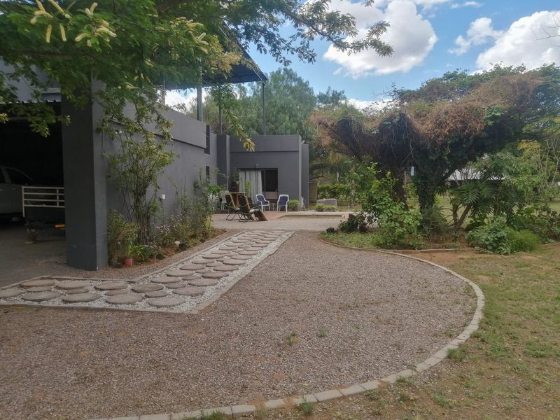 Rear exterior view of the property featuring a modern dark-painted structure, a paved stone walkway, and a gravel garden area.