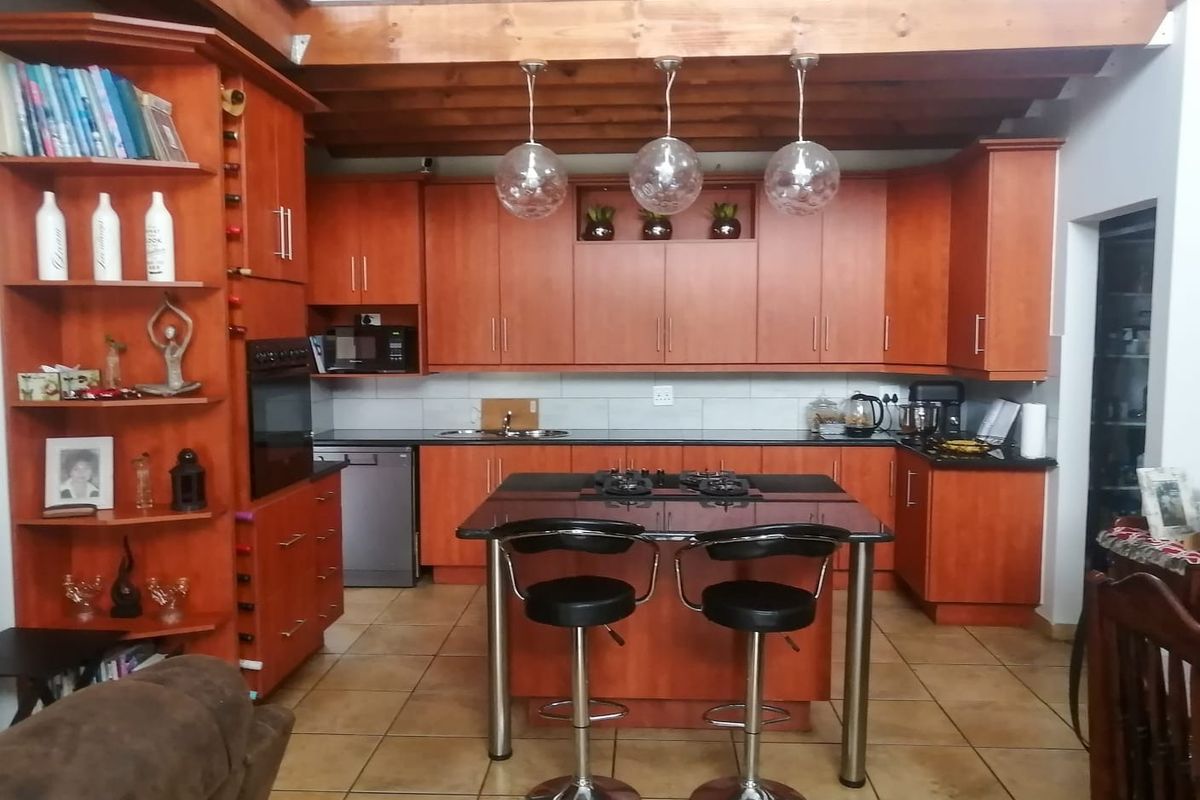 A well-appointed kitchen featuring warm-toned cabinetry, a central island with a gas hob, tiled flooring, and exposed timber ceiling beams.