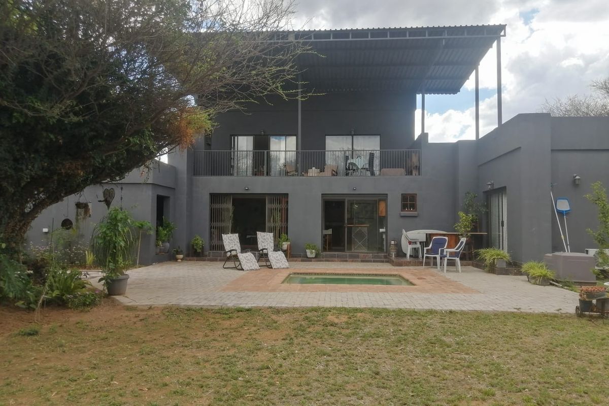 Rear view of a two-story dwelling featuring a paved patio area, a small swimming pool, and an upper-level balcony with metal roofing.