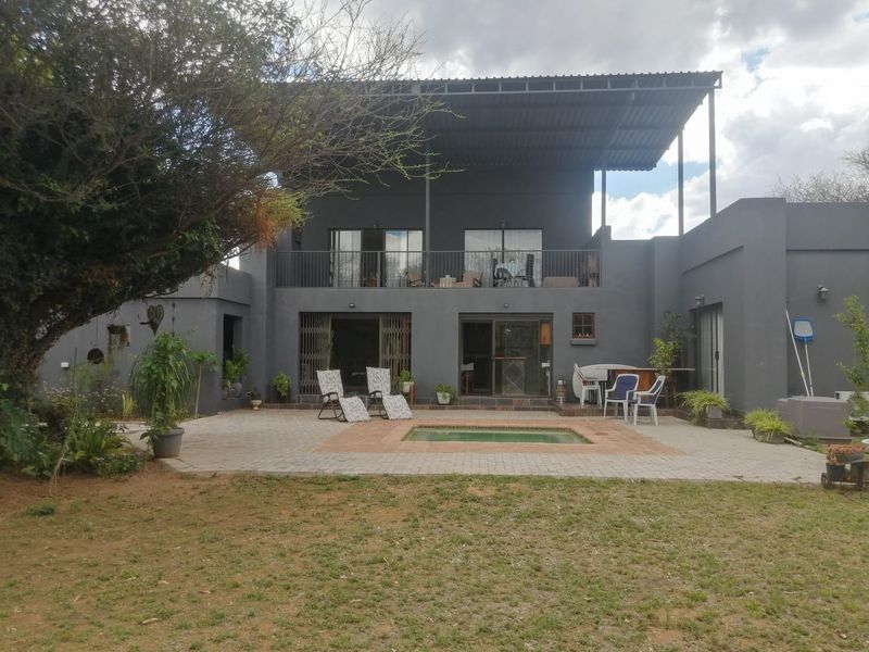 Rear view of a two-story dwelling featuring a paved patio area, a small swimming pool, and an upper-level balcony with metal roofing.