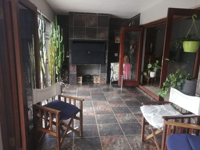 Covered patio area featuring a built-in braai, dark tiled flooring, and timber door frames leading to the interior living space.