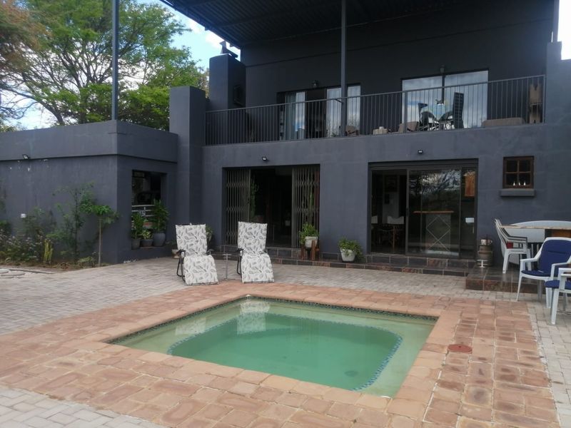 Rear exterior view featuring a swimming pool with brick paving, a covered patio area, and an upper-level balcony with metal railings.