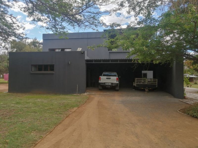 Front elevation of a modern grey-painted dwelling featuring a spacious covered carport area and a gravel driveway.