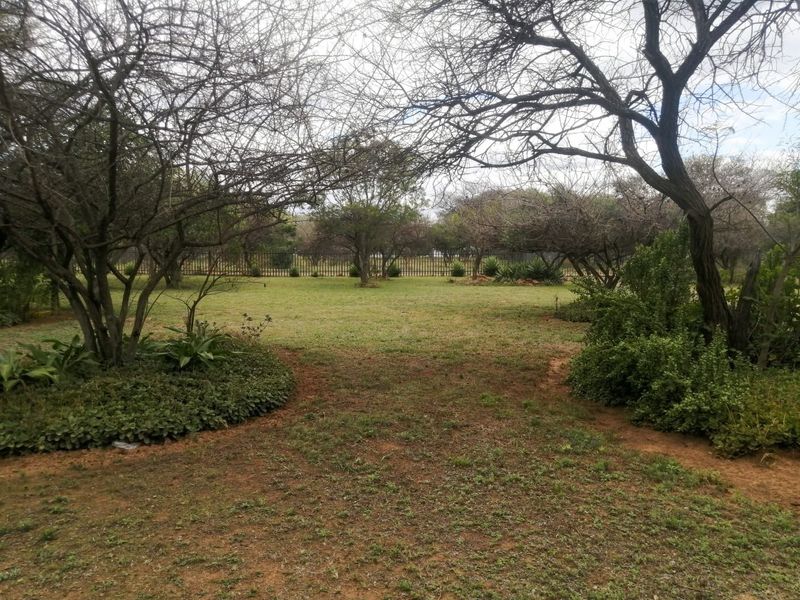 A spacious, well-established garden area featuring mature trees, natural landscaping, and secure perimeter fencing on the small holding property.