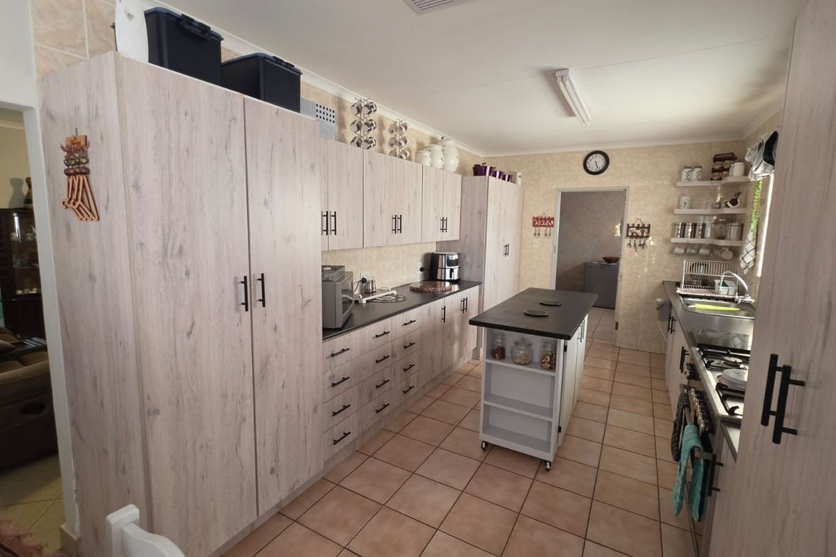 A functional kitchen featuring light wood-grain cabinetry, a central island, tiled flooring, and a gas hob with a tiled backsplash.