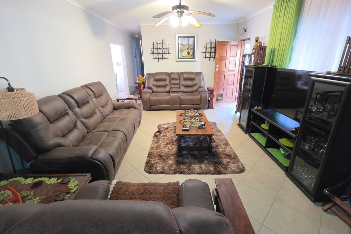 A spacious living room featuring tiled flooring, a central ceiling fan, and a timber entrance door, providing a functional and comfortable living space.