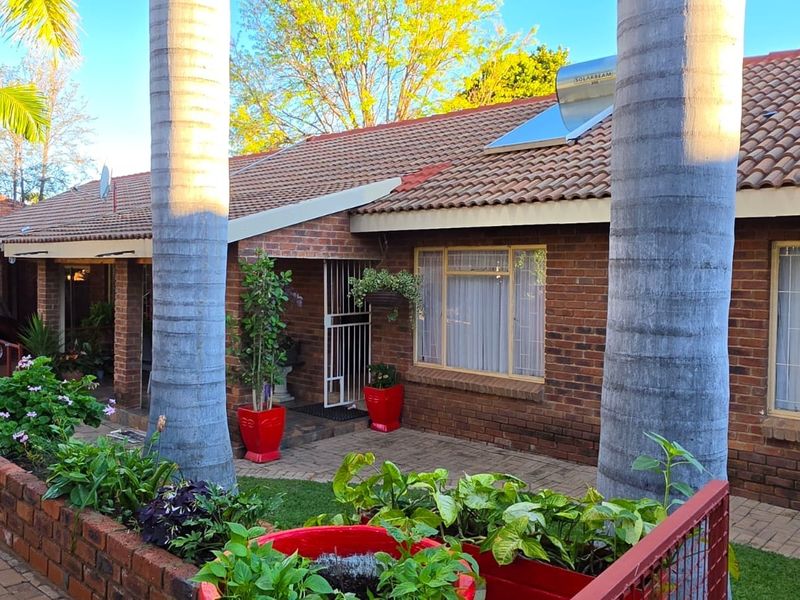 A charming brick-faced home featuring a tiled roof, solar water heating system, and a well-maintained paved entrance area with established garden beds.