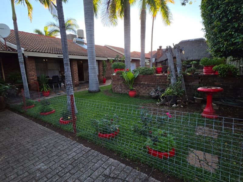 Rear garden area featuring a brick facade, tiled roof, paved walkway, and a brick retaining wall with established landscaping.