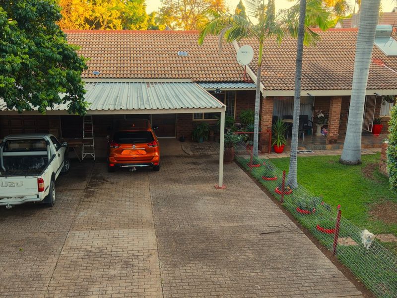 Front exterior view of the property featuring a paved driveway, a covered carport, and a tiled roof with solar water heating infrastructure.