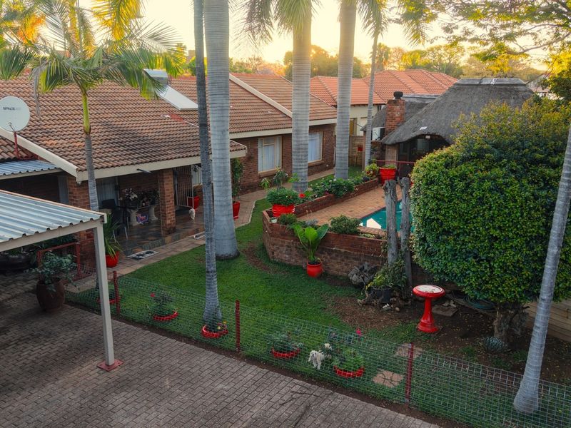 Elevated view of the rear garden featuring a swimming pool, thatched lapa, covered patio, and established landscaping with mature palm trees.