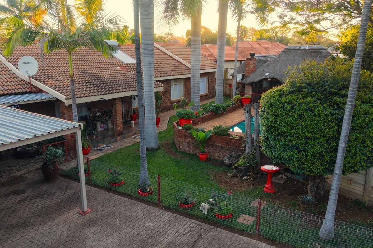 Elevated view of the rear garden featuring a swimming pool, thatched lapa, covered patio, and established landscaping with mature palm trees.
