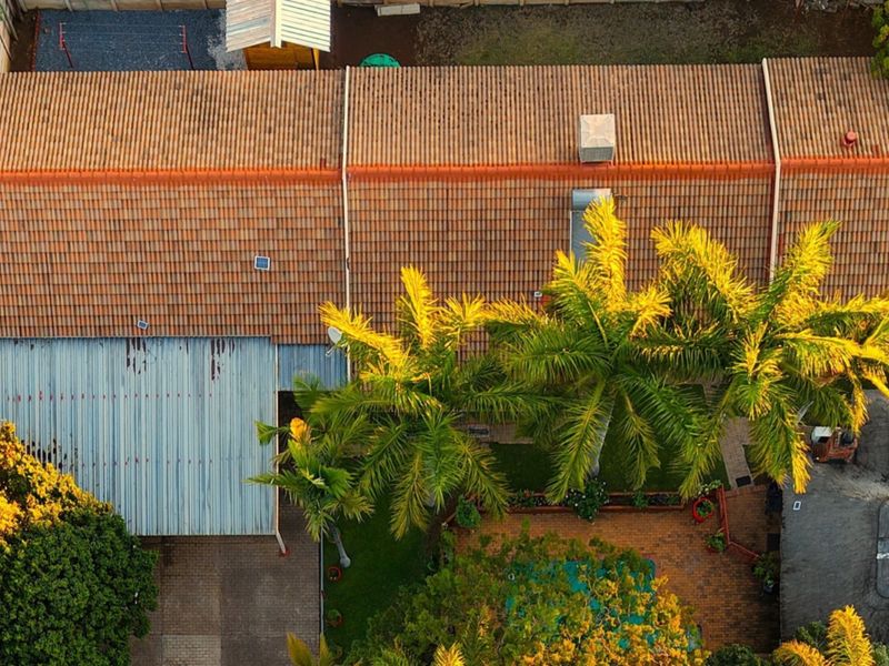 Aerial view of the property showing the tiled roof, corrugated metal roof section, swimming pool, and paved outdoor entertainment area.