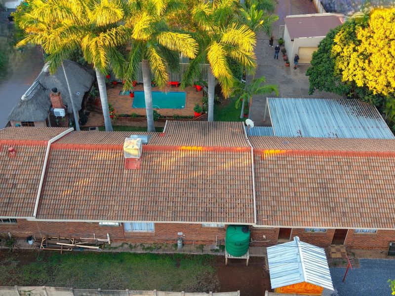 Aerial view of the property featuring a tiled roof house, swimming pool, thatched lapa, and a spacious backyard with a water tank.