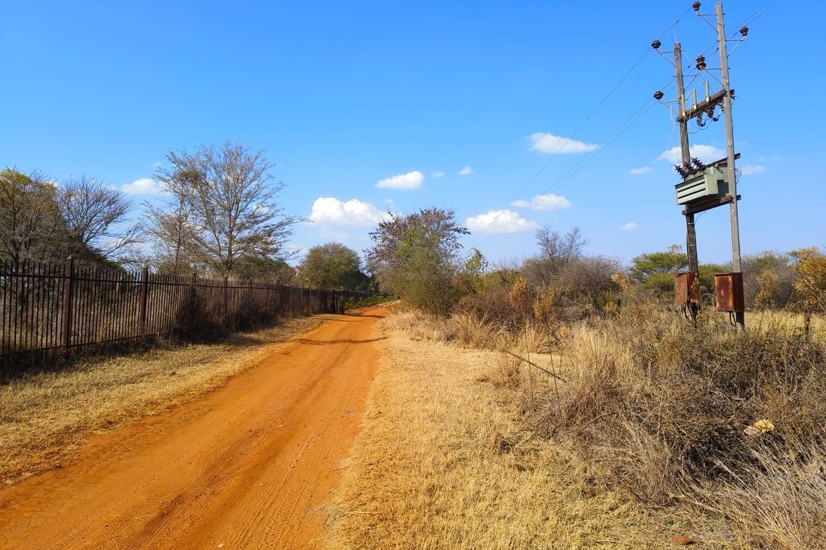 A view of a dirt access road bordering a property with metal fencing and an existing utility pole with an electrical transformer.