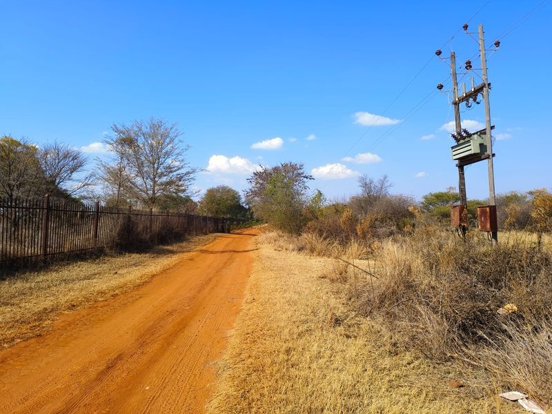 A view of a dirt access road bordering a property with metal fencing and an existing utility pole with an electrical transformer.
