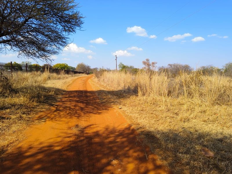 A view of a dirt access road leading through the vacant residential land, featuring perimeter fencing and natural vegetation.