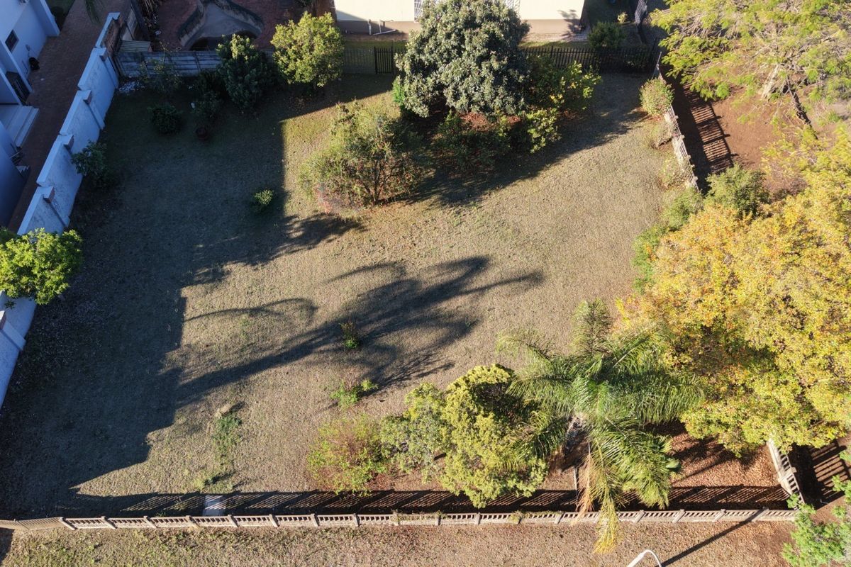 An aerial view of a residential vacant land plot featuring established trees and perimeter fencing, offering a clear perspective of the property boundaries.