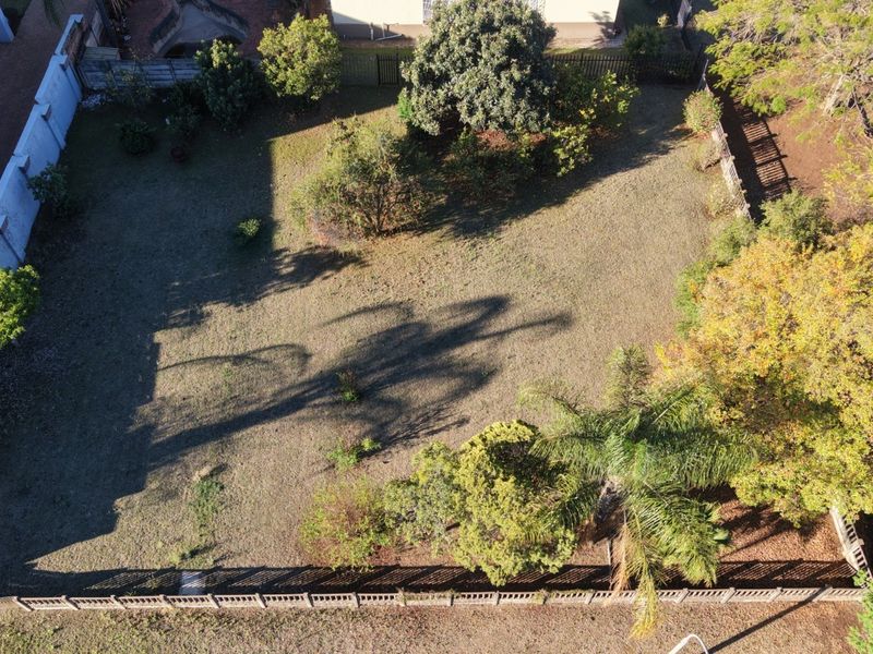 An aerial view of a residential vacant land plot featuring established trees and perimeter fencing, offering a clear perspective of the property boundaries.