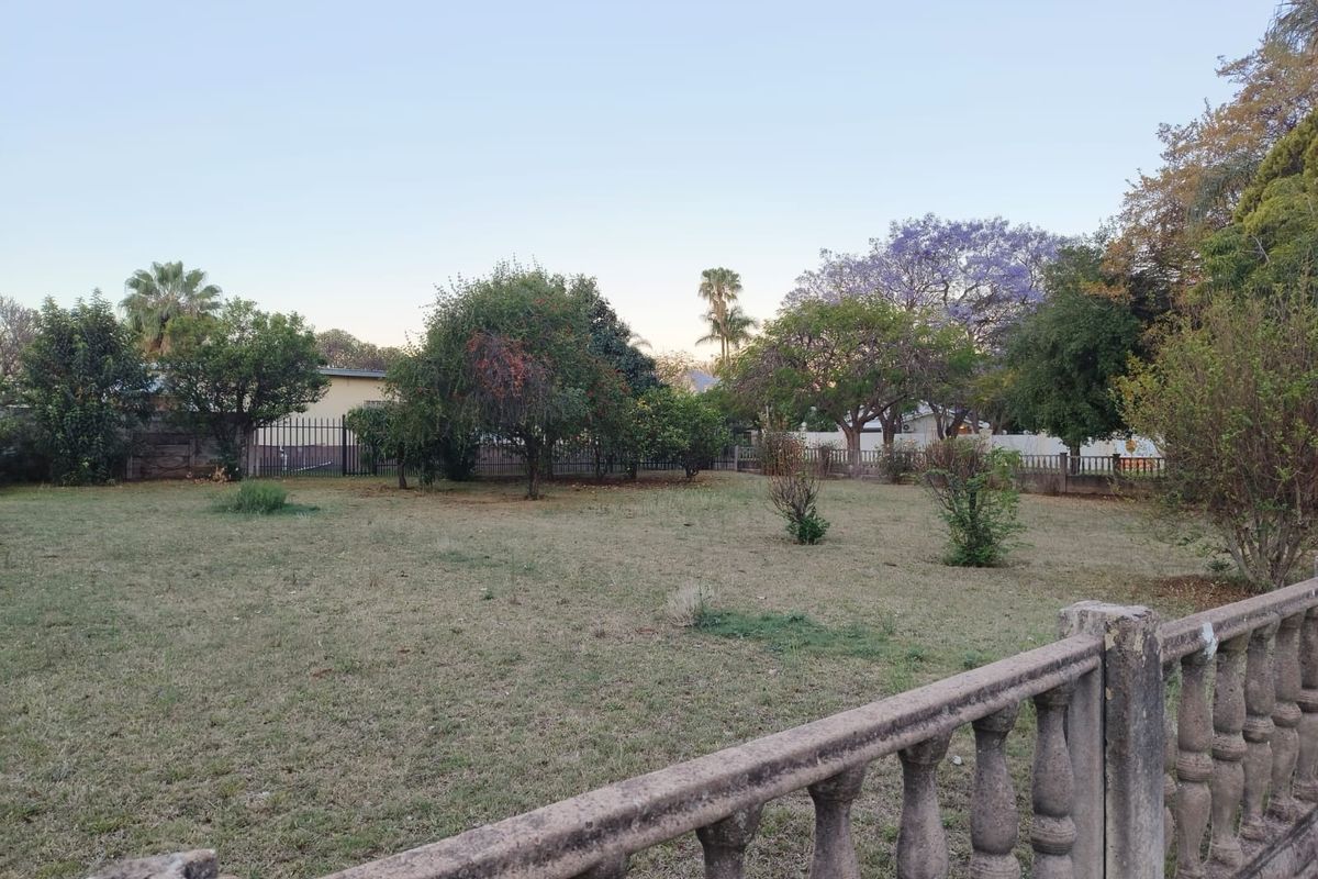 A spacious residential plot featuring established trees, a concrete balustrade boundary wall, and metal perimeter fencing.