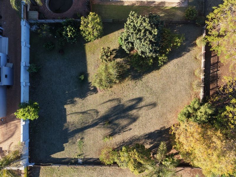 Aerial view of a residential vacant land plot featuring established trees and perimeter fencing.