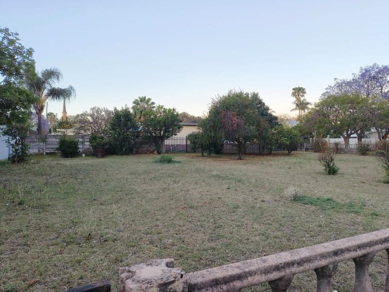 A spacious residential garden plot featuring mature trees, perimeter fencing, and a weathered concrete balustrade in the foreground.