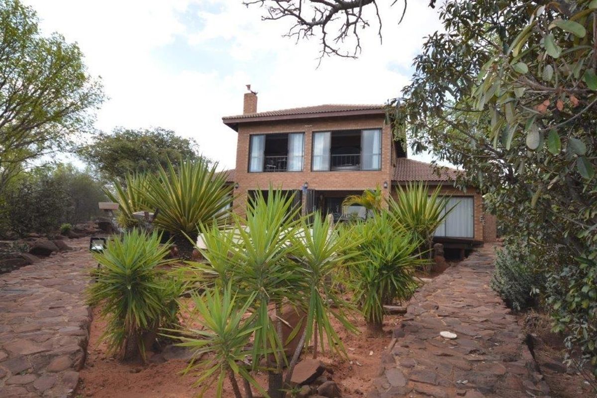 A two-story brick house featuring a tiled roof, chimney, and sliding glass doors, set within a landscaped garden with stone pathways.