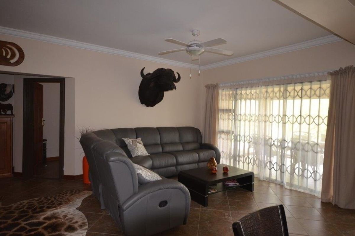 A comfortable living room featuring tiled flooring, a ceiling fan, and a large sliding glass door with a security gate providing access to the outdoors.