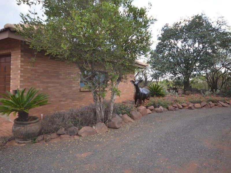 Front exterior view of a brick house featuring a garage entrance, gravel driveway, and landscaped rock garden border.